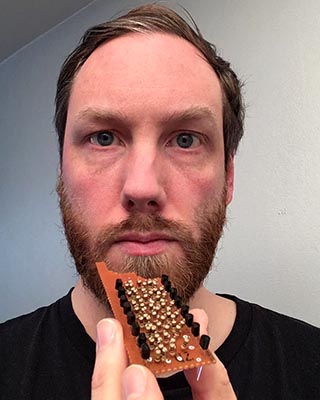 Picture of me holding a piece of veroboard stuffed with resistors and transistors. One edge of the board is uneven which implies that I might have taken a bite out of it